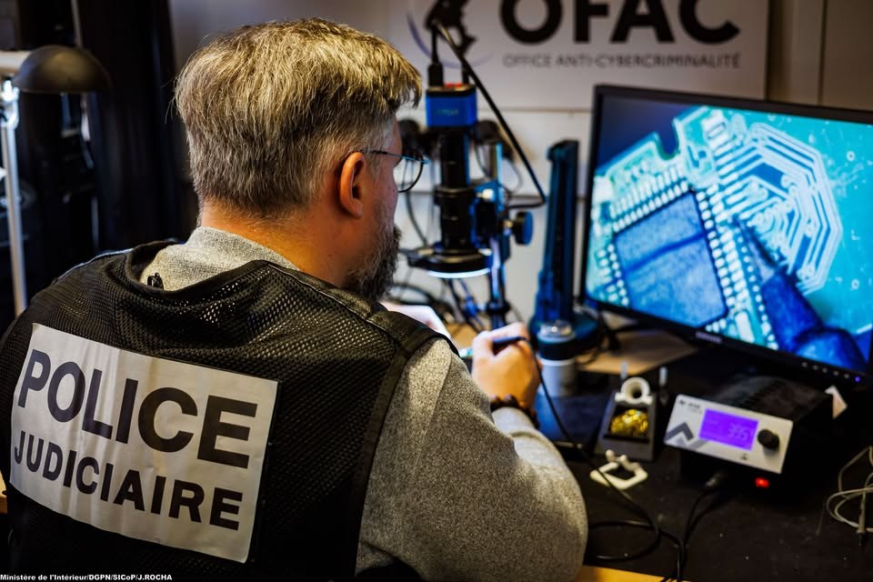 Un enquêteur de la police judiciaire analyse une carte électronique sur un écran, sous le bandeau de l'Office anti-cybercriminalité