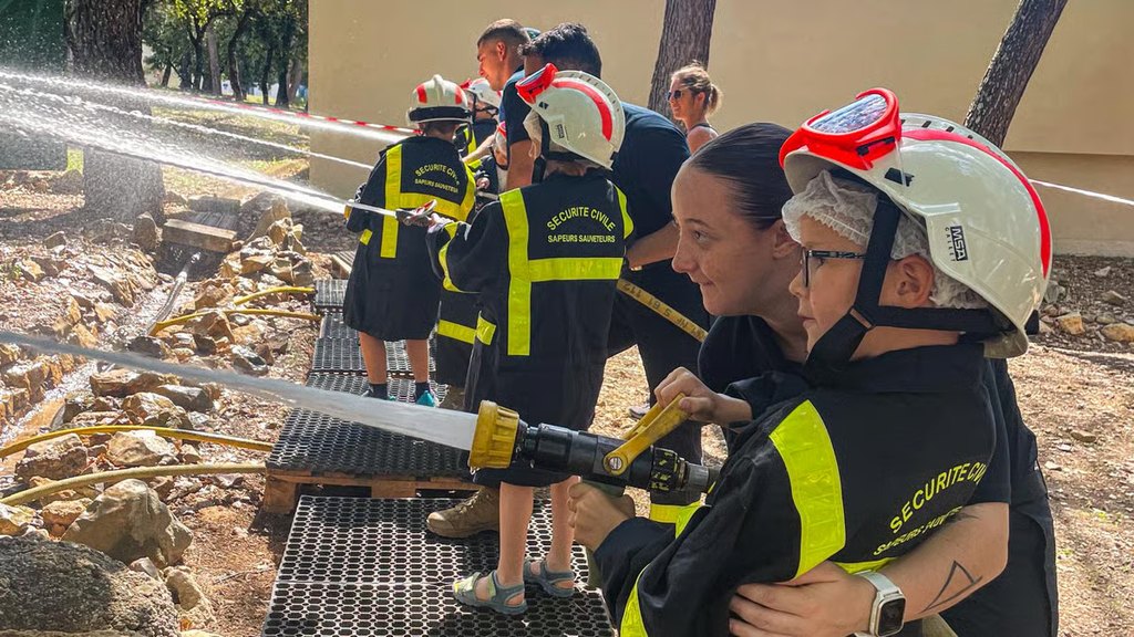 Des enfants manœuvrent une lance à incendie avec des sapeurs-sauveteurs de la sécurité civile