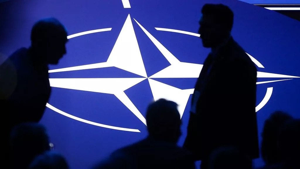 Silhouettes de participants devant le logo de l'OTAN projeté sur un mur bleu